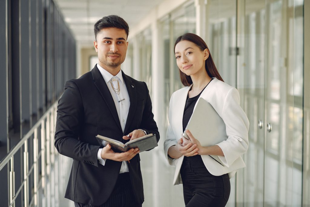 pexels photo 4173356 4173356 Confident well dressed multiracial coworkers standing in modern office corridor while holding laptop and notebook in hands and looking at camera
