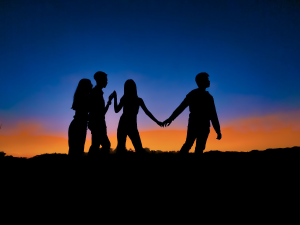 A group of friends holding hands, silhouetted against a vibrant sunset sky.