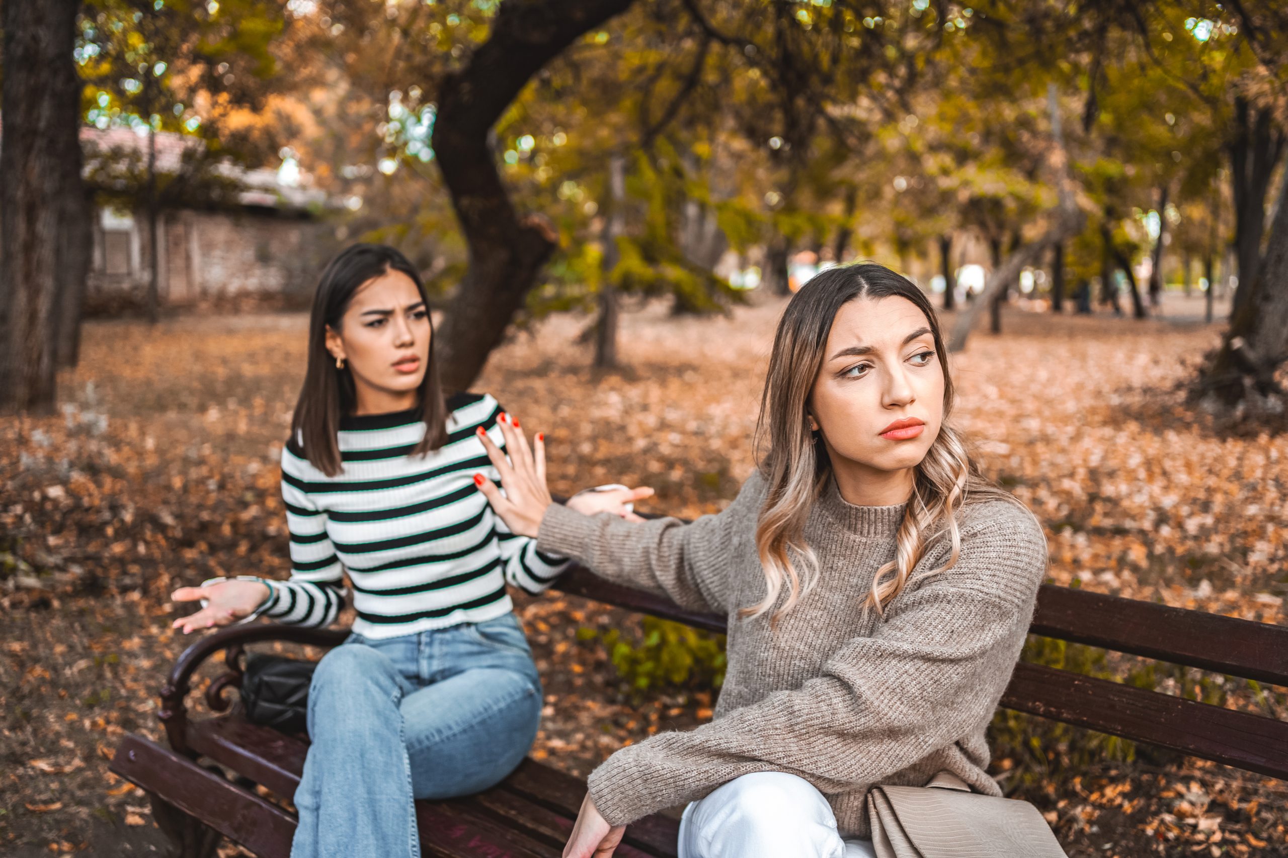two women are sitting on a bench and one does not want to listen to the other anymore
